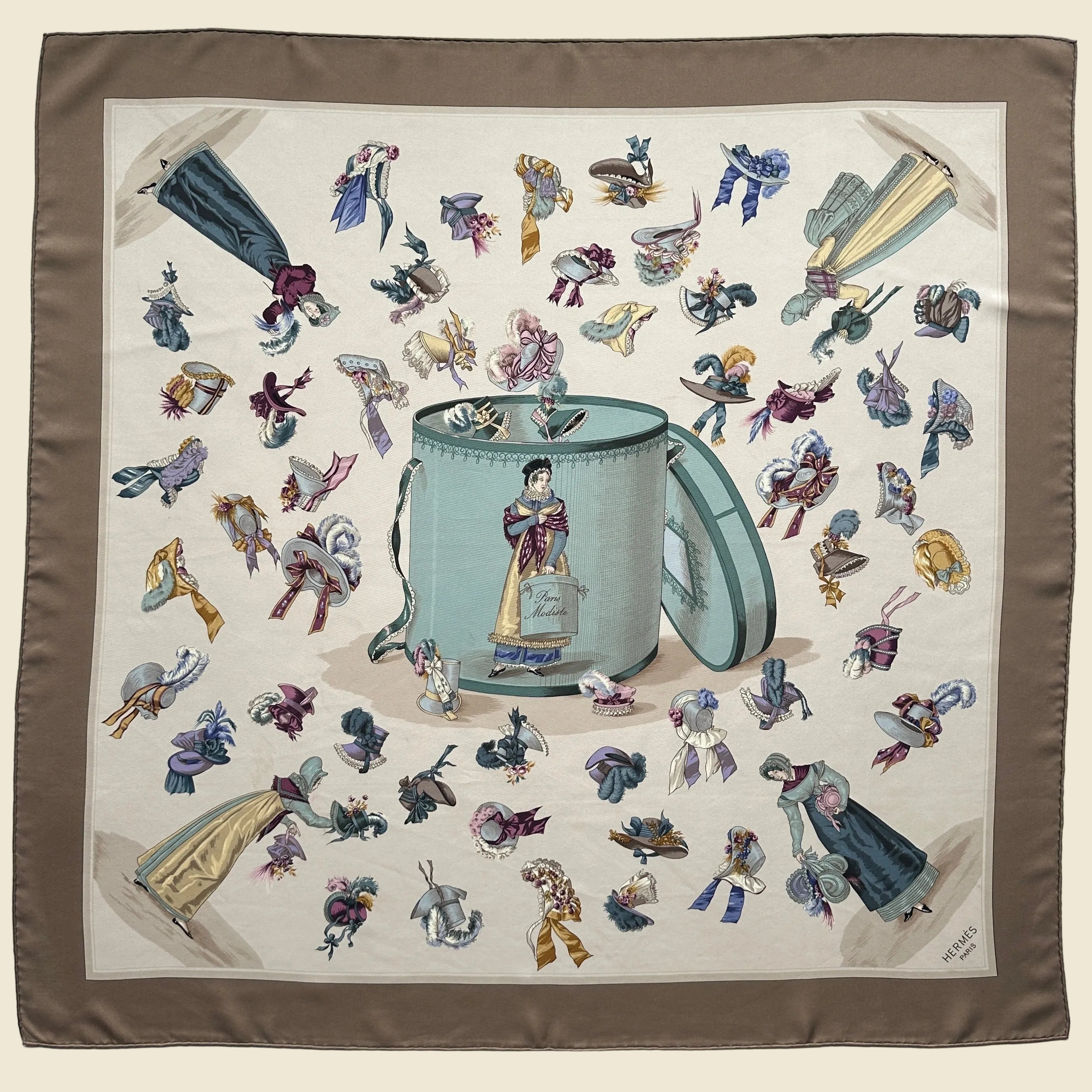 Carré Hermès "Paris Modiste" (1956) première édition, fond crème et bordure marron, motif central de boîte à chapeaux et farandole de coiffes anciennes.